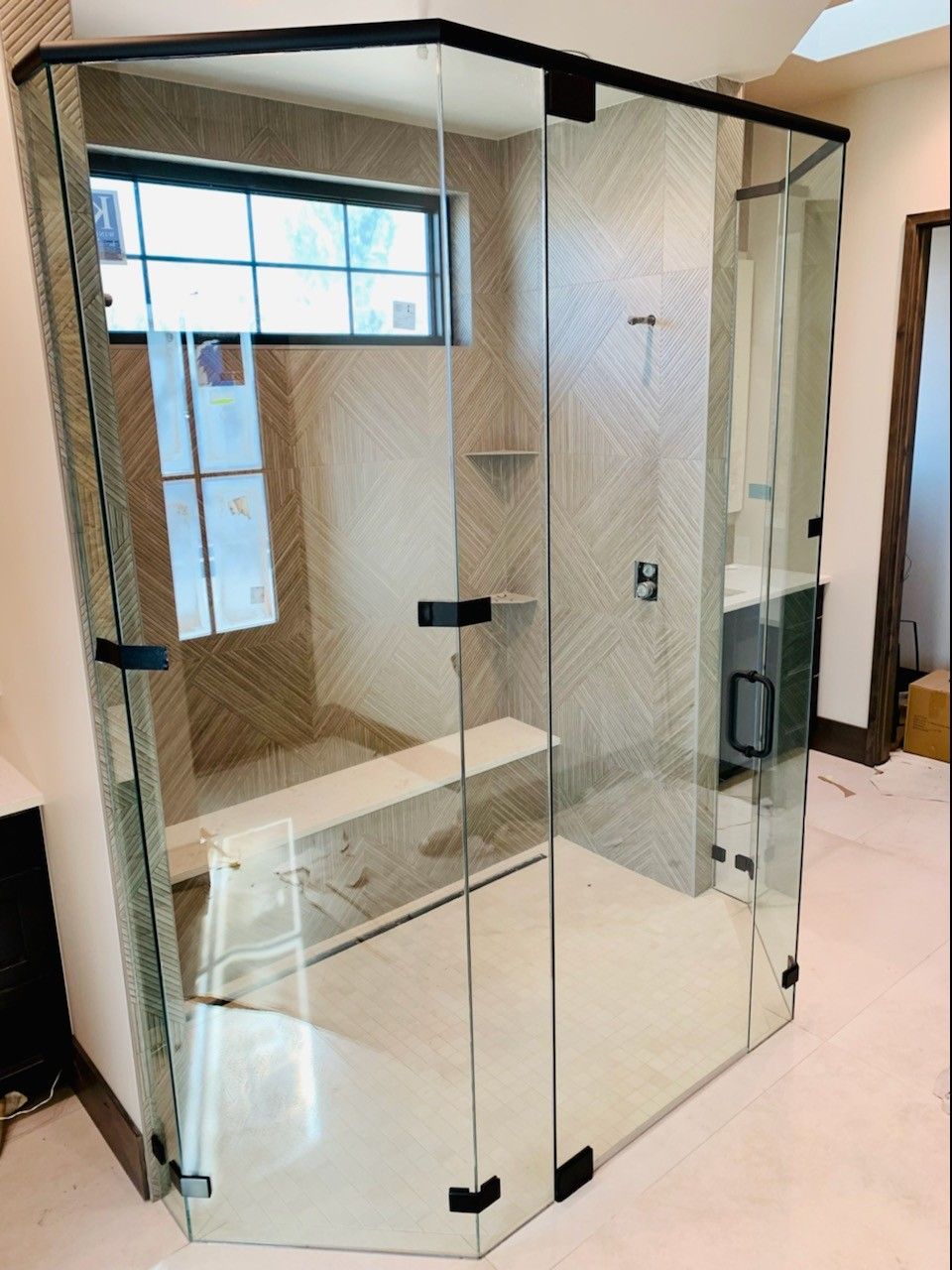 Glass walk-in shower with black trim, built-in bench, and tiled walls in a bathroom
