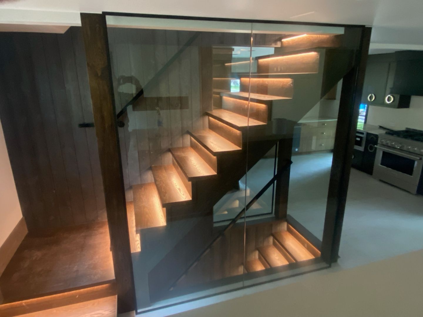 Modern glass staircase with warm wooden treads and built-in lighting inside a sleek home interior