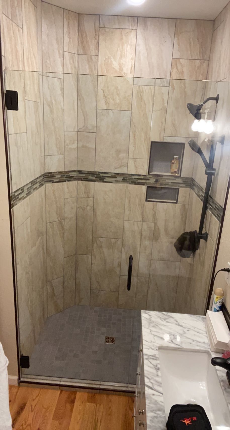 Small tiled walk-in shower with gray floor, built-in shelf, and black shower fixtures.