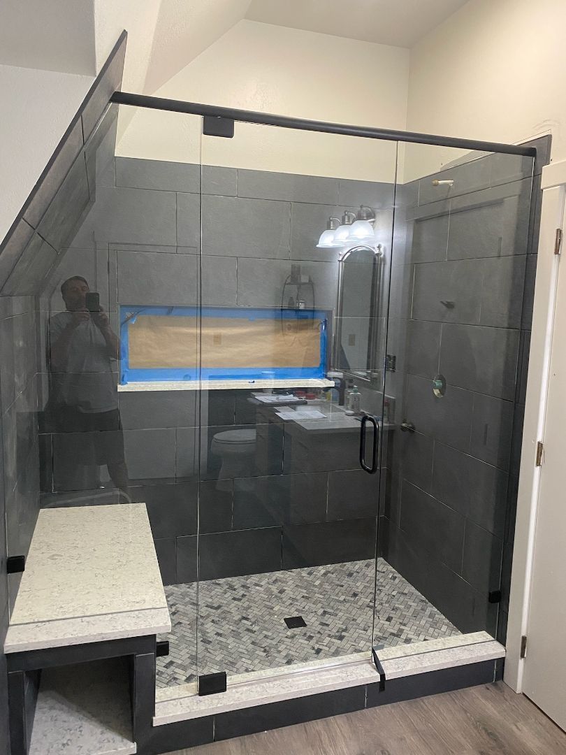 Modern glass shower enclosure with tiled walls, bench seat, and pebble-pattern floor in a bathroom
