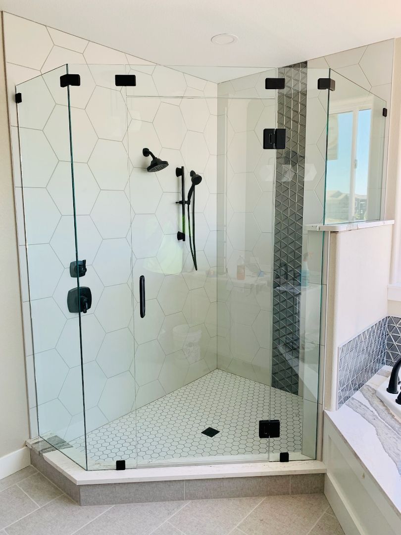 Glass walk-in shower with hex tile floor, white walls, black fixtures, and chrome shower controls