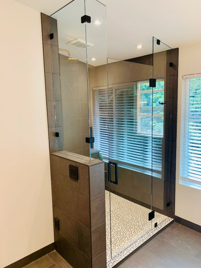Glass-walled shower with beige stone tile and a small vanity in a modern bathroom