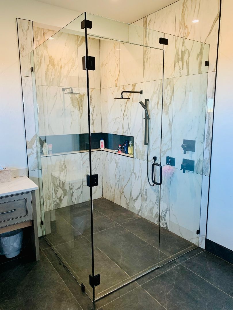 Glass shower enclosure with black hinges and marble-pattern tile walls in a modern bathroom