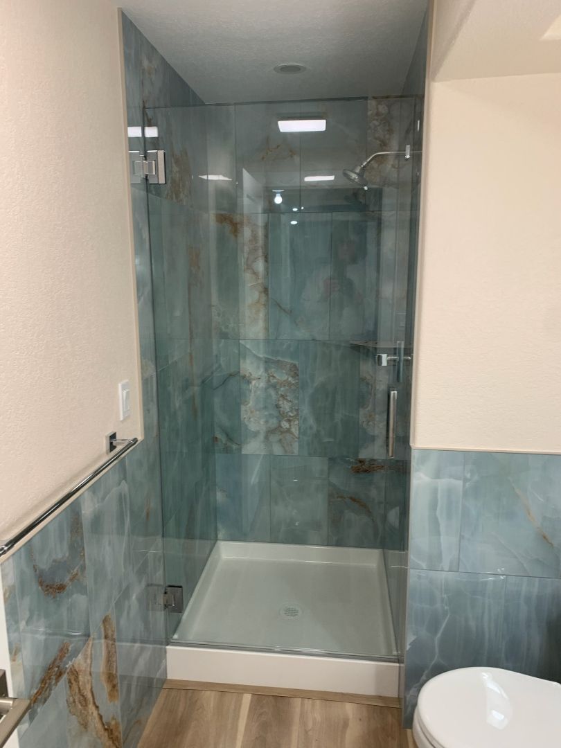 Glass shower enclosure in a small bathroom with beige and blue tile walls.