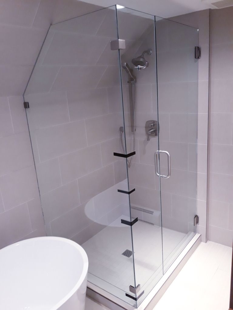 Glass walk-in shower with black hinges and white tiled walls in a bright bathroom
