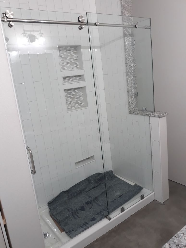 Glass shower enclosure with chrome hardware and gray floor mat in a bathroom