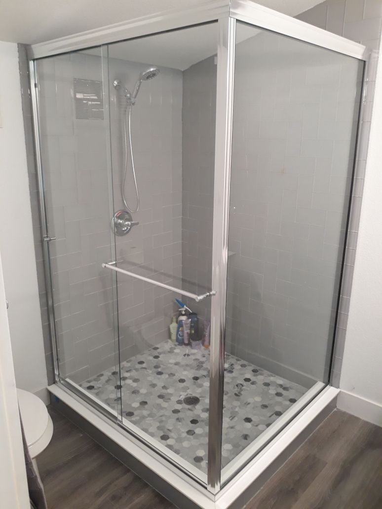 Glass shower stall with chrome frame and patterned tile floor in a bathroom