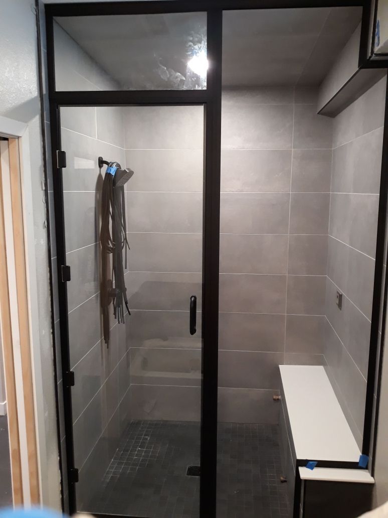 Glass shower enclosure with black frame, gray tile walls, and a white bench inside.