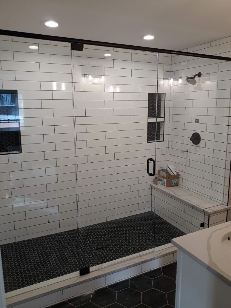 Modern bathroom with white subway tile, black accents, a shower bench, and glass shower enclosure