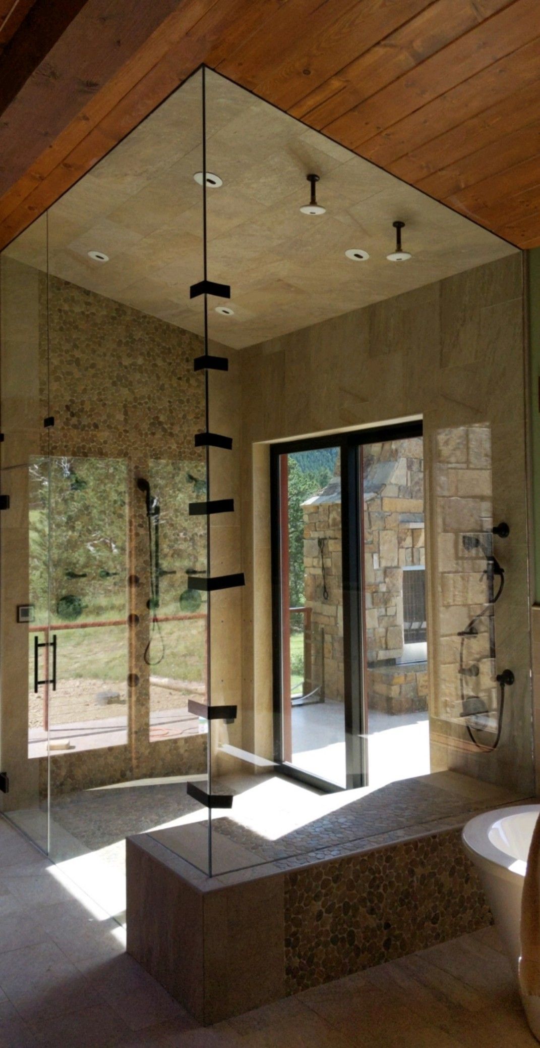 Modern bathroom with a large walk-in shower, glass door, and tan tiled walls under a wood ceiling.