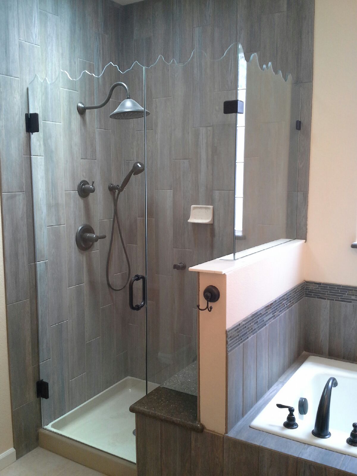 Modern bathroom with a walk-in shower, glass enclosure, and wood-look tile walls; bathtub edge in foreground