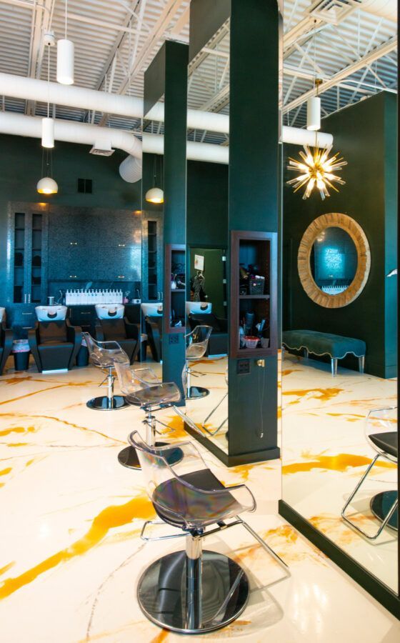Modern salon interior with black styling chairs, tall mirrored columns, and yellow paint splatters on the floor