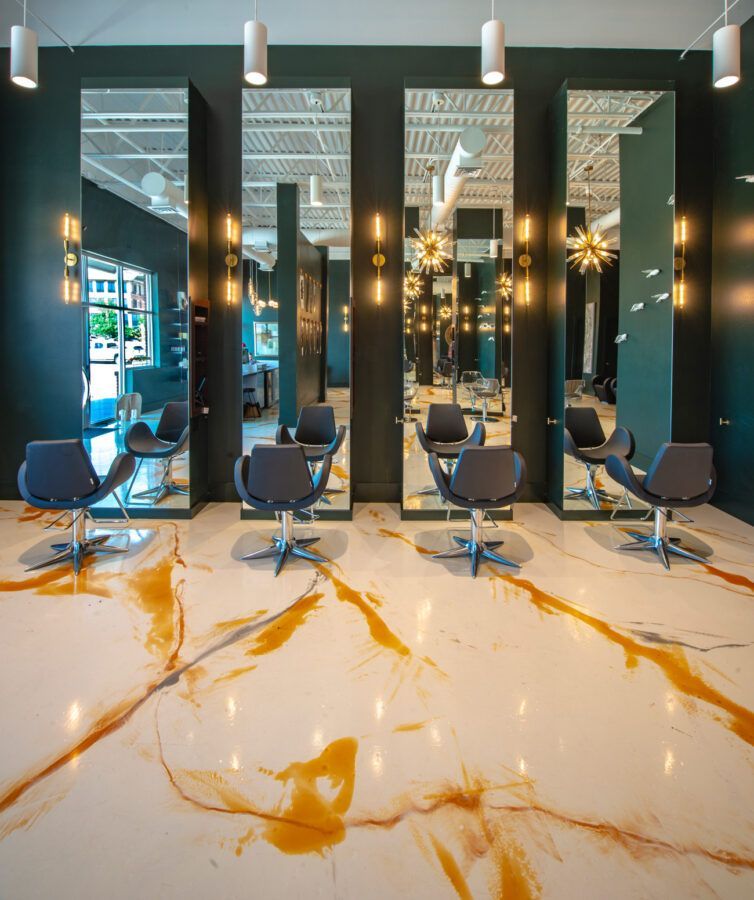 Modern salon interior with styling chairs, mirrors, and black walls, featuring a glossy white-and-gold marble floor