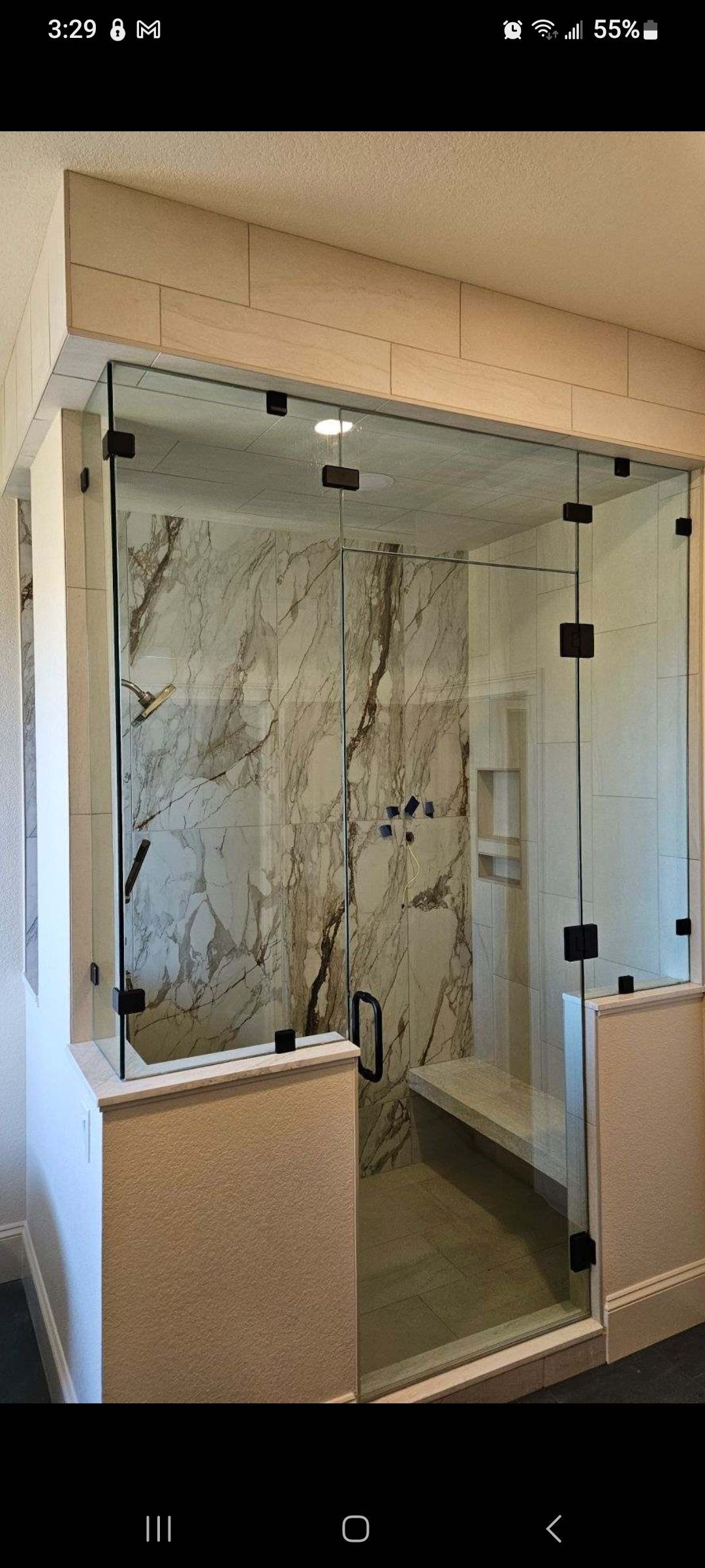 Glass walk-in shower with marble walls, black hardware, and beige stone trim