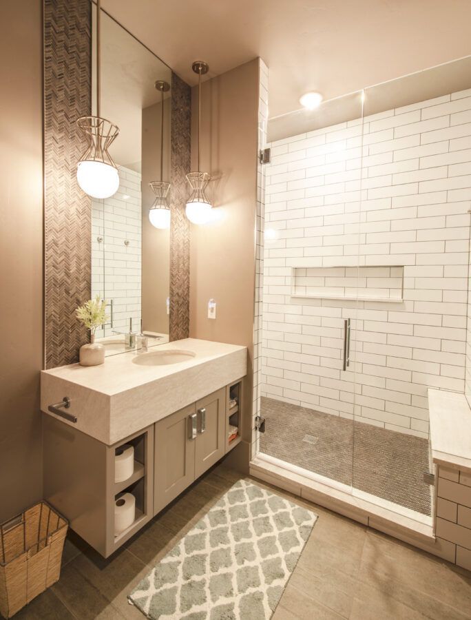Modern bathroom with white subway-tile shower, vanity sink, large mirror, and patterned rug