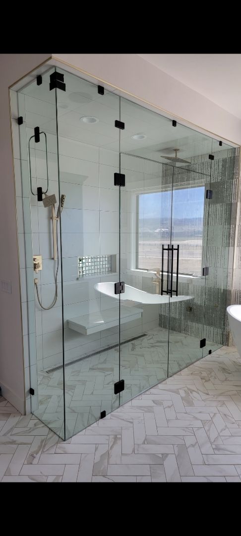 Glass-walled shower enclosure in a bright, modern bathroom with white tile flooring.