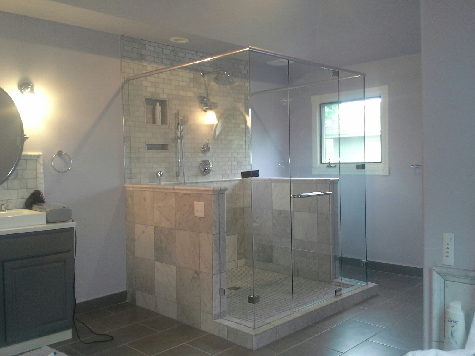 Walk-in shower with clear glass enclosure, beige tile, and a small window in a modern bathroom.