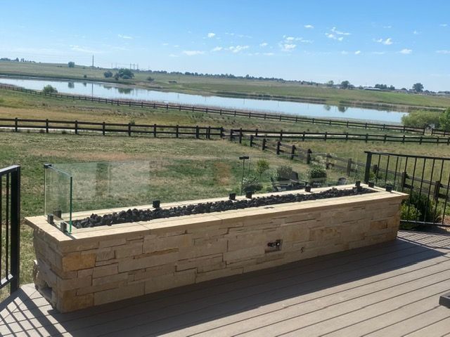 Stone planter on a wooden deck overlooking a fenced grassy pond landscape.