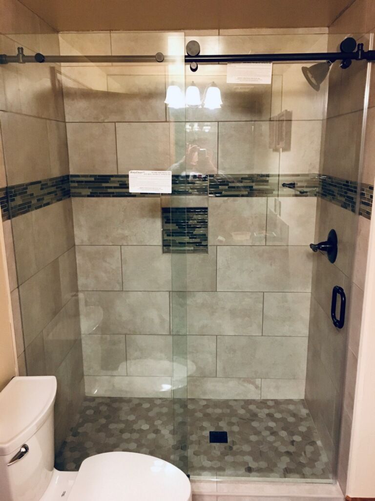Walk-in shower with glass door, beige tile walls, and patterned pebble floor in a bathroom