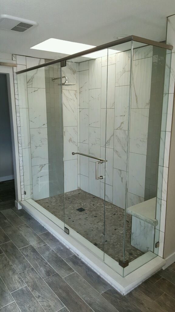 White-framed walk-in shower enclosure with speckled tile floor in a modern bathroom.