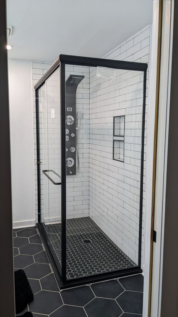 Modern glass shower enclosure with black trim in a white-tiled bathroom