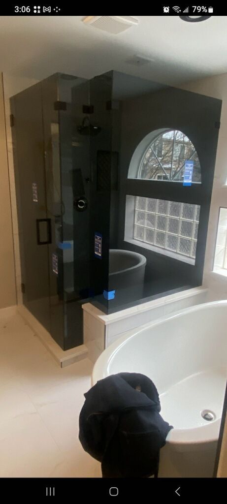 Modern bathroom with a glass shower enclosure, white tub, and arched window reflection