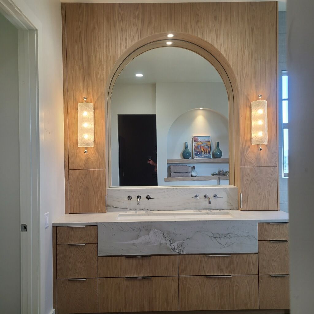 Modern bathroom vanity with arched wood-framed mirror, marble countertop, and wall sconces