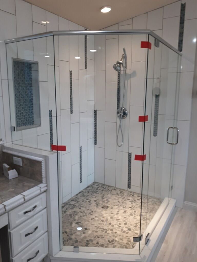 Glass shower stall with chrome fixtures, pebble tile floor, and white subway walls in a bathroom