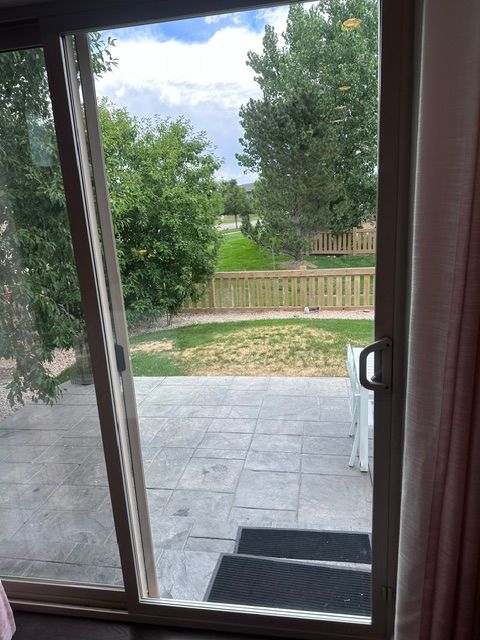 Sliding glass door opening to a patio, lawn, and trees beyond a wooden fence
