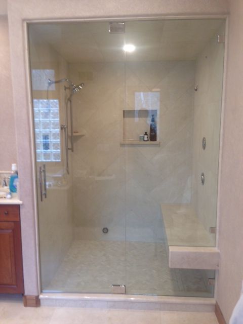 Glass shower enclosure in a beige bathroom with a built-in bench and overhead light.