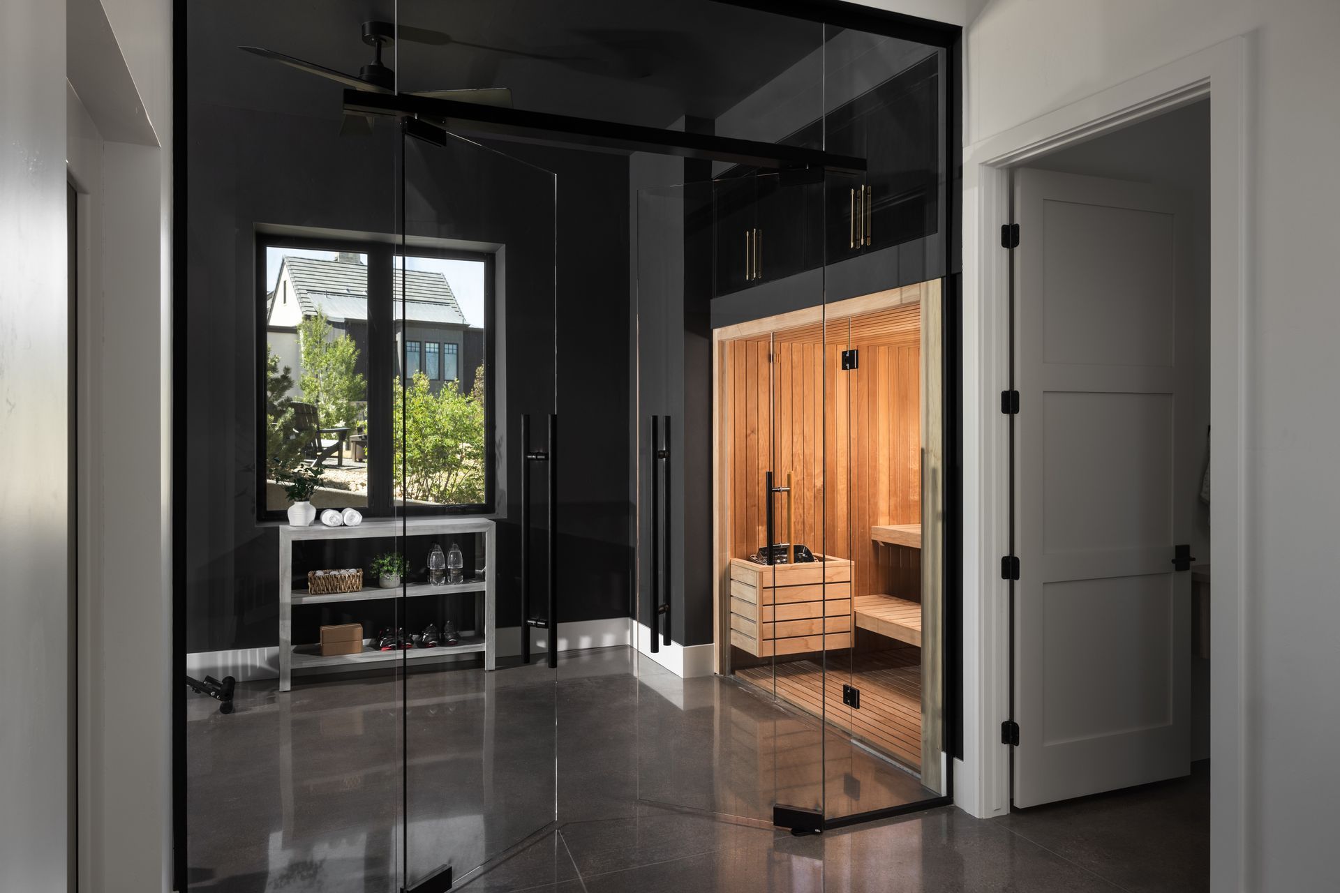 Modern bathroom with glossy black walls, a lit wooden sauna, and a large window view outdoors