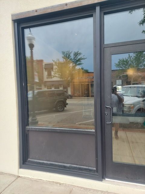 Empty storefront with dark-framed glass door and window reflecting parked cars and street scene