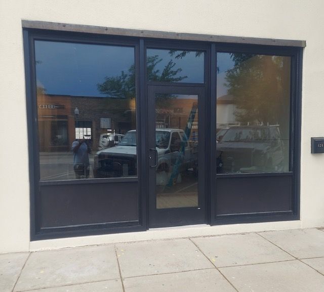 Dark-tinted storefront windows and a glass door reflecting parked vehicles and a sidewalk