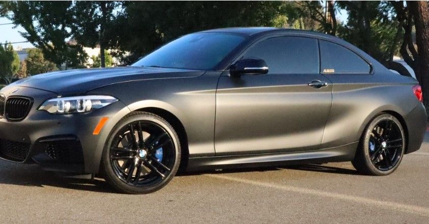 Dark gray BMW coupe with black rims and tinted windows parked outside.