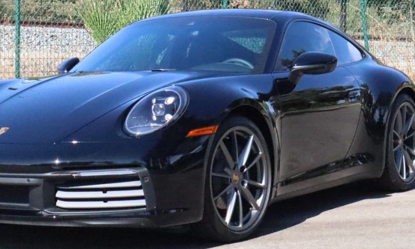 Black Porsche 911 coupe parked outdoors with sunlight reflecting on the glossy paint.