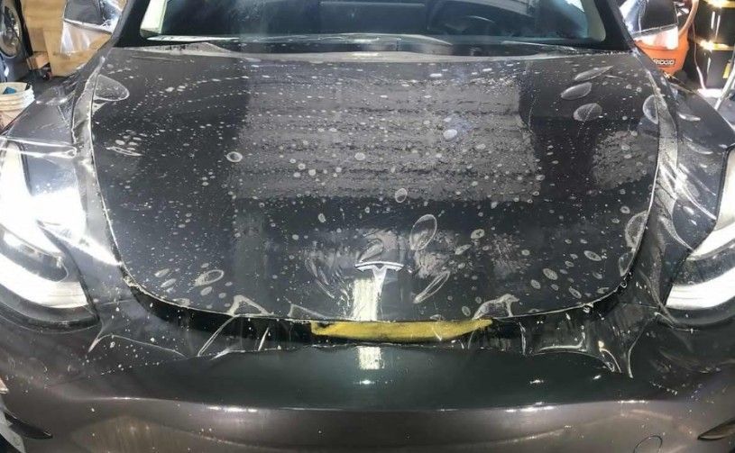A Tesla car with a protective film applied to its hood. The film is clear with air bubbles.