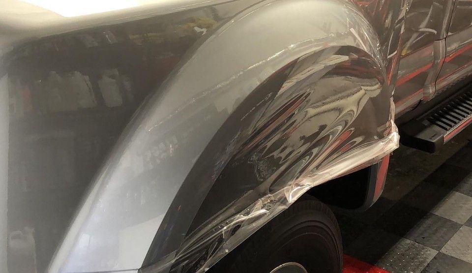 A gray pickup truck fender wrapped in clear protective film.