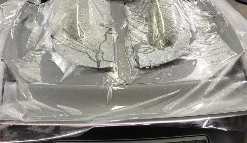 Kitchen scale wrapped in plastic. Silver base, white surface with dark markings.