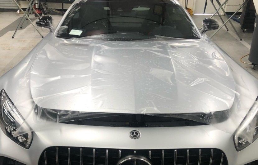 Silver car hood covered in protective plastic in a shop.