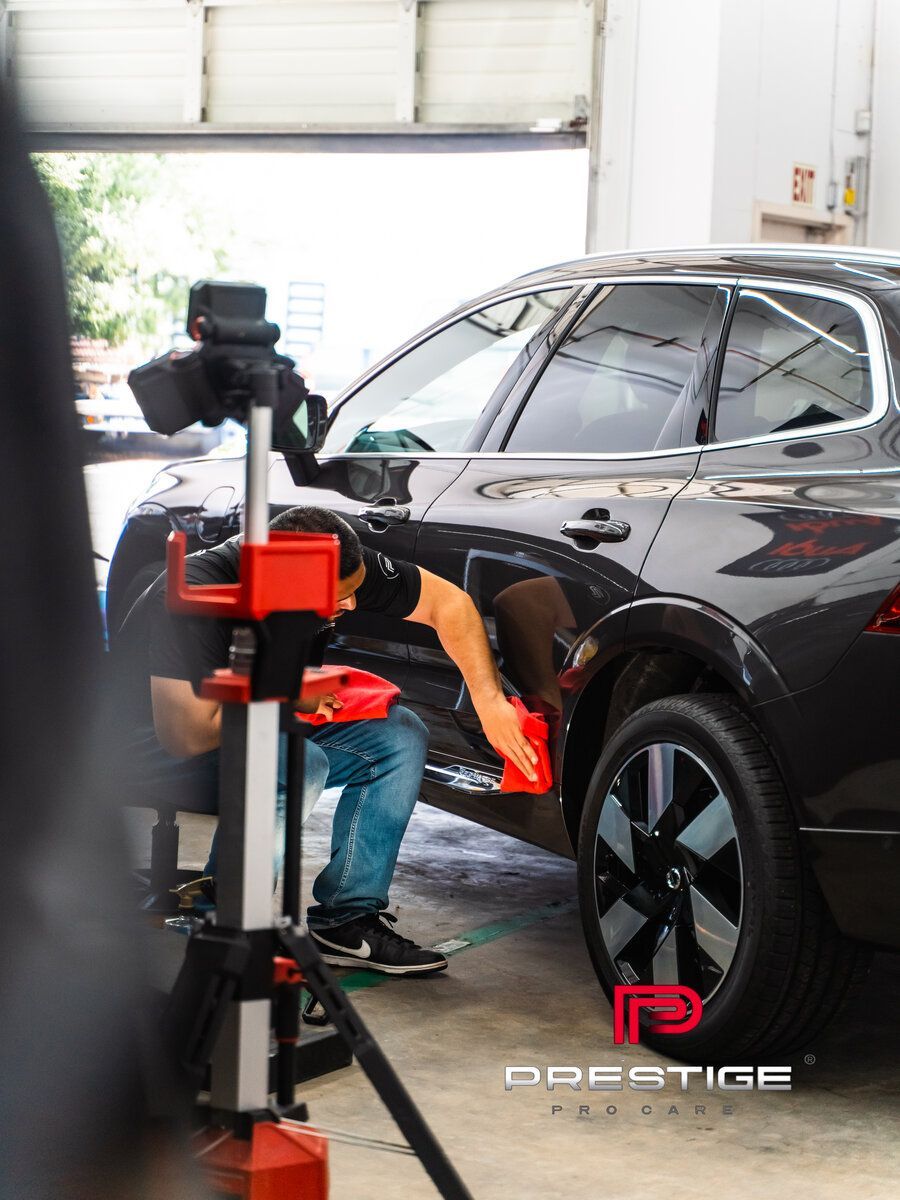 Mechanic working on a black SUV in a garage, using a red machine near the front wheel.