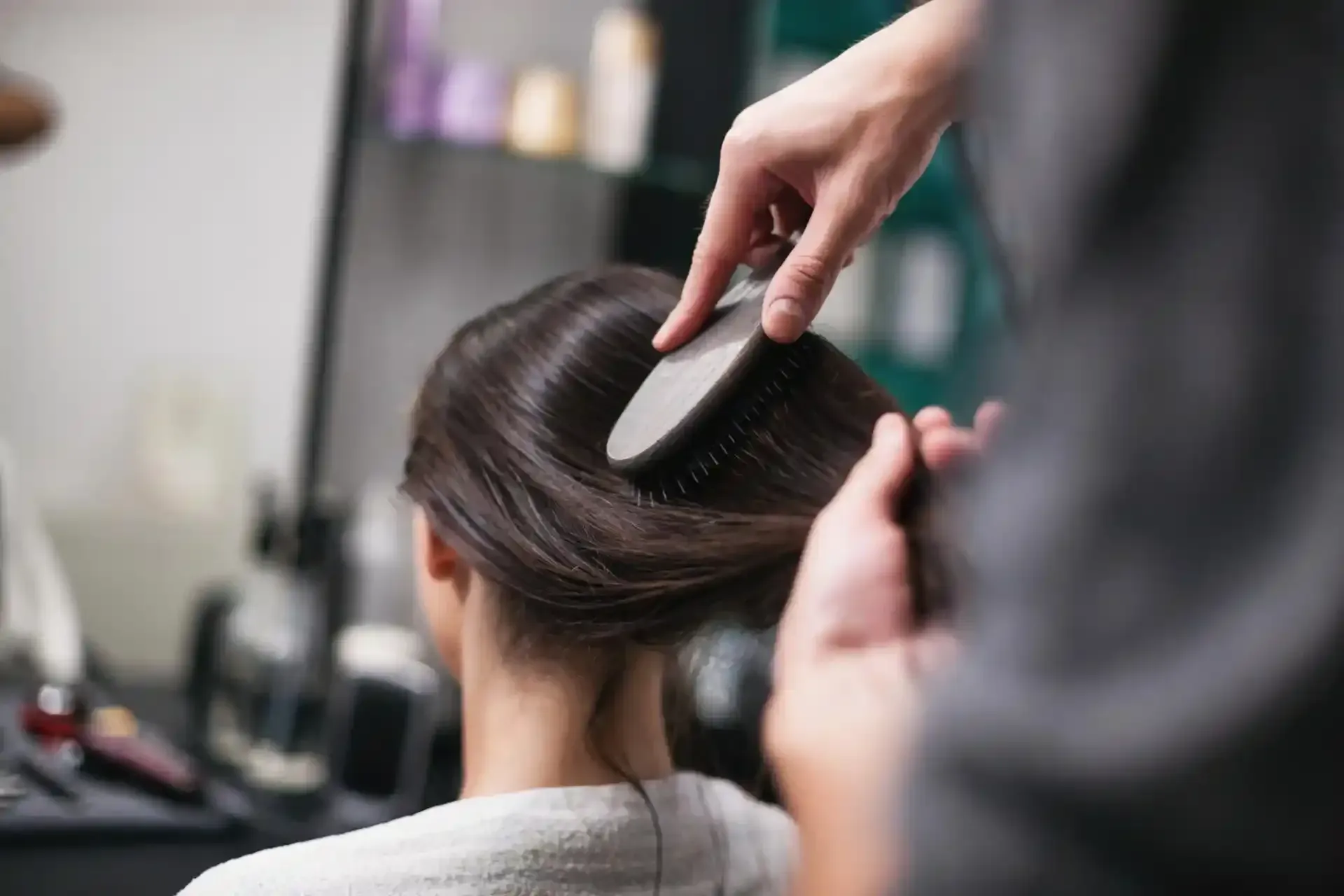 I capelli di una persona vengono acconciati con una spazzola in un salone di bellezza, con le mani del parrucchiere visibili.