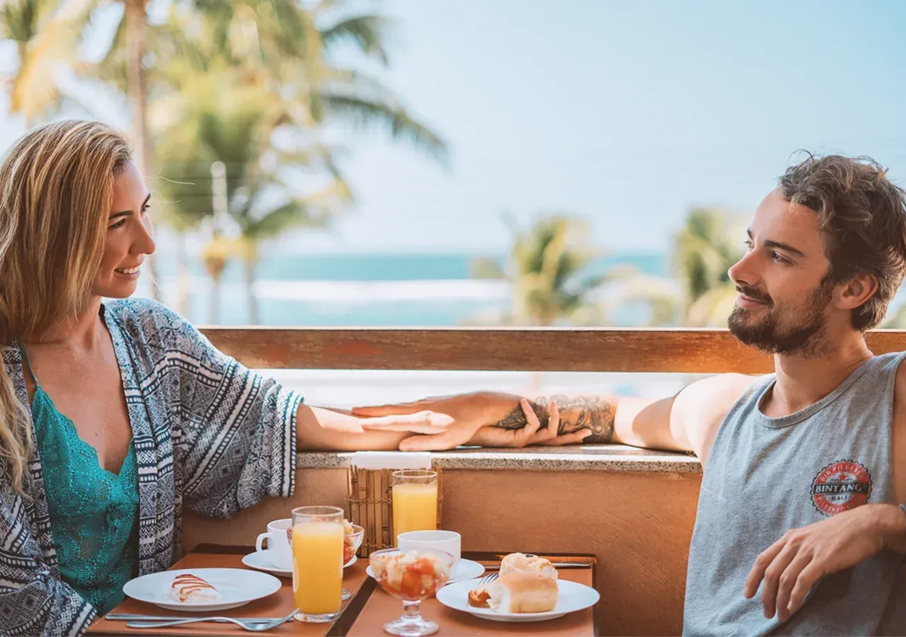 Um homem e uma mulher estão sentados à mesa com pratos de comida e bebidas.