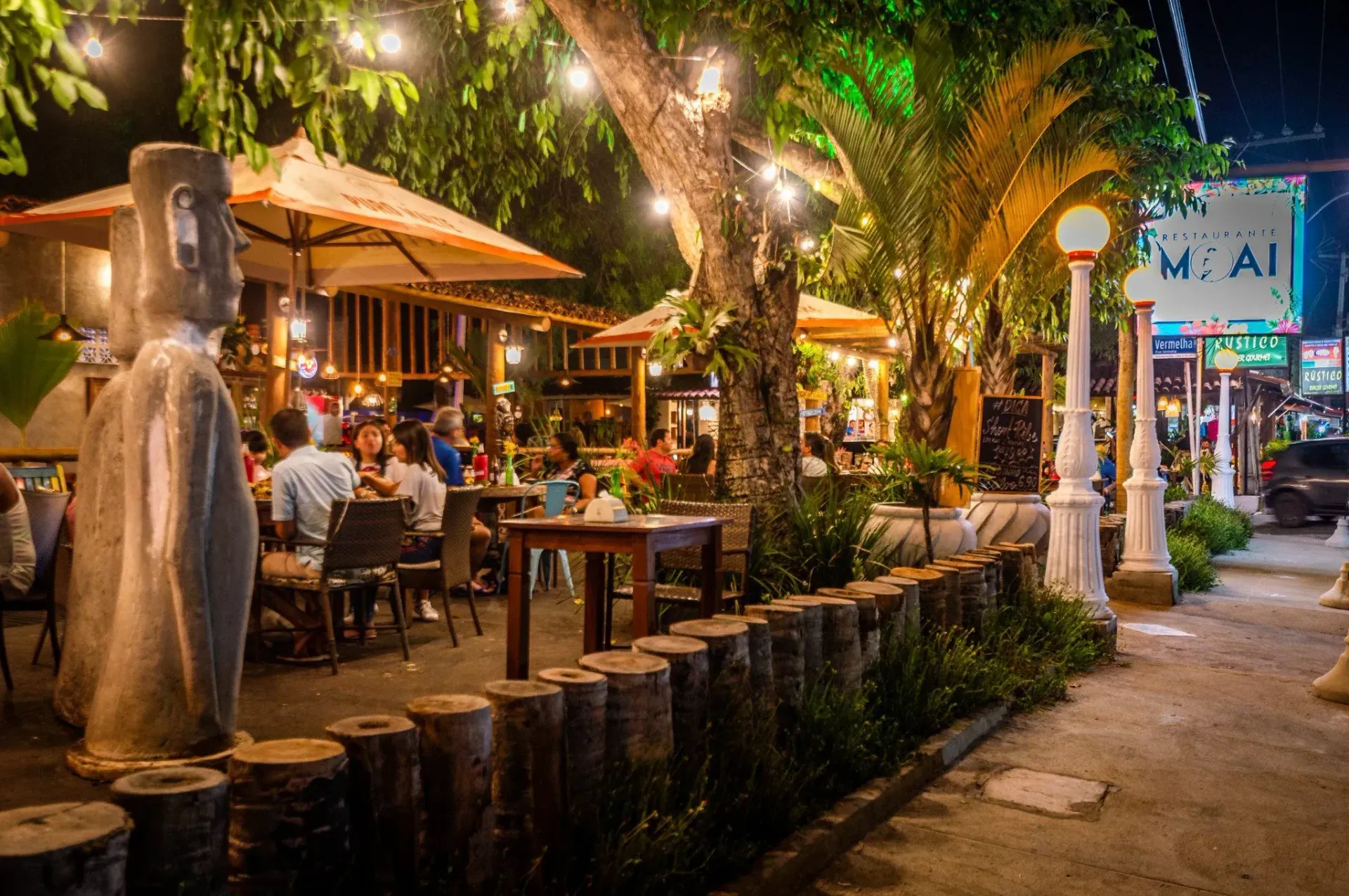 Um grupo de pessoas está sentado em mesas do lado de fora de um restaurante à noite.