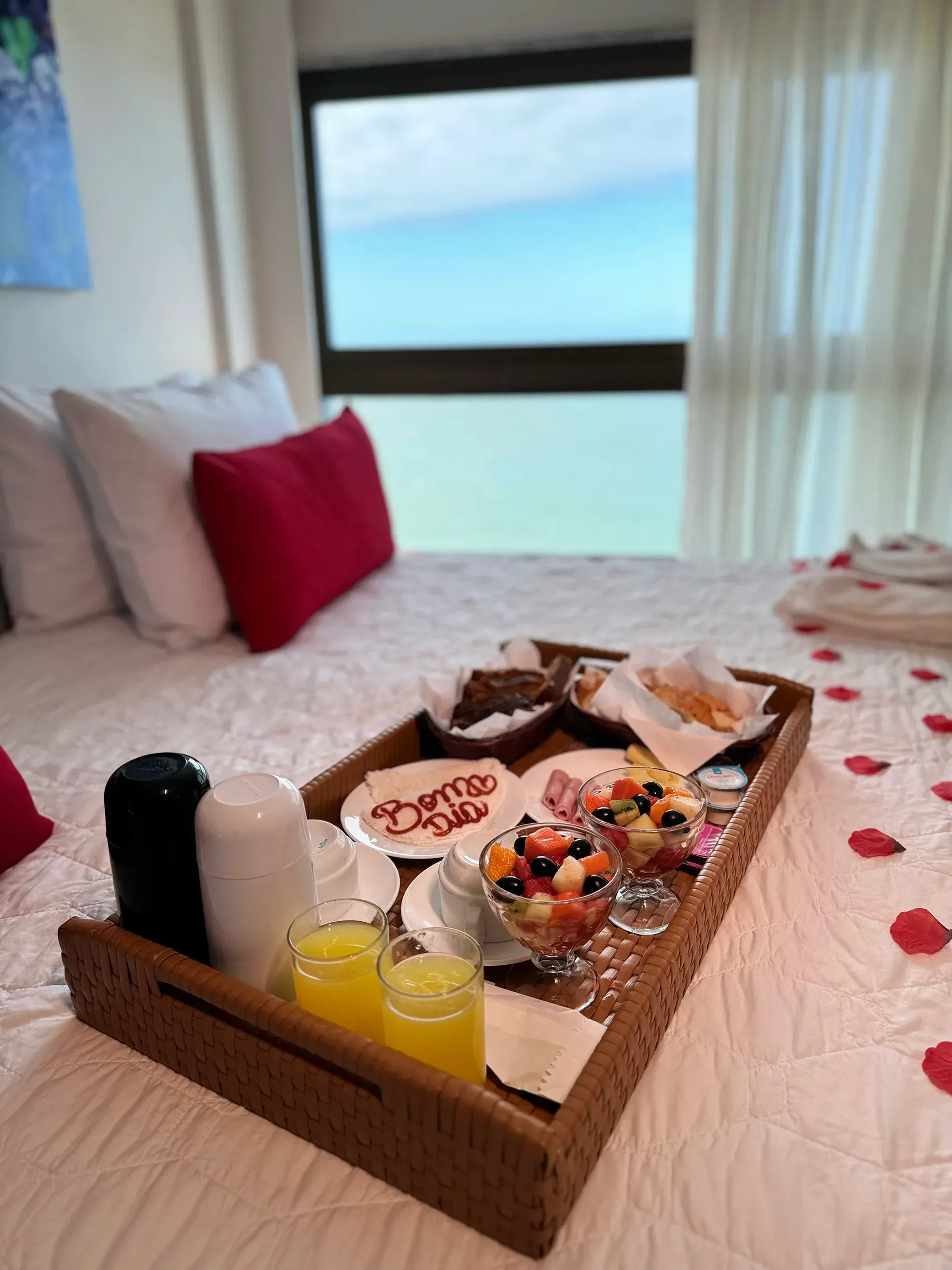 Uma bandeja de comida está sobre uma cama em frente a uma janela.