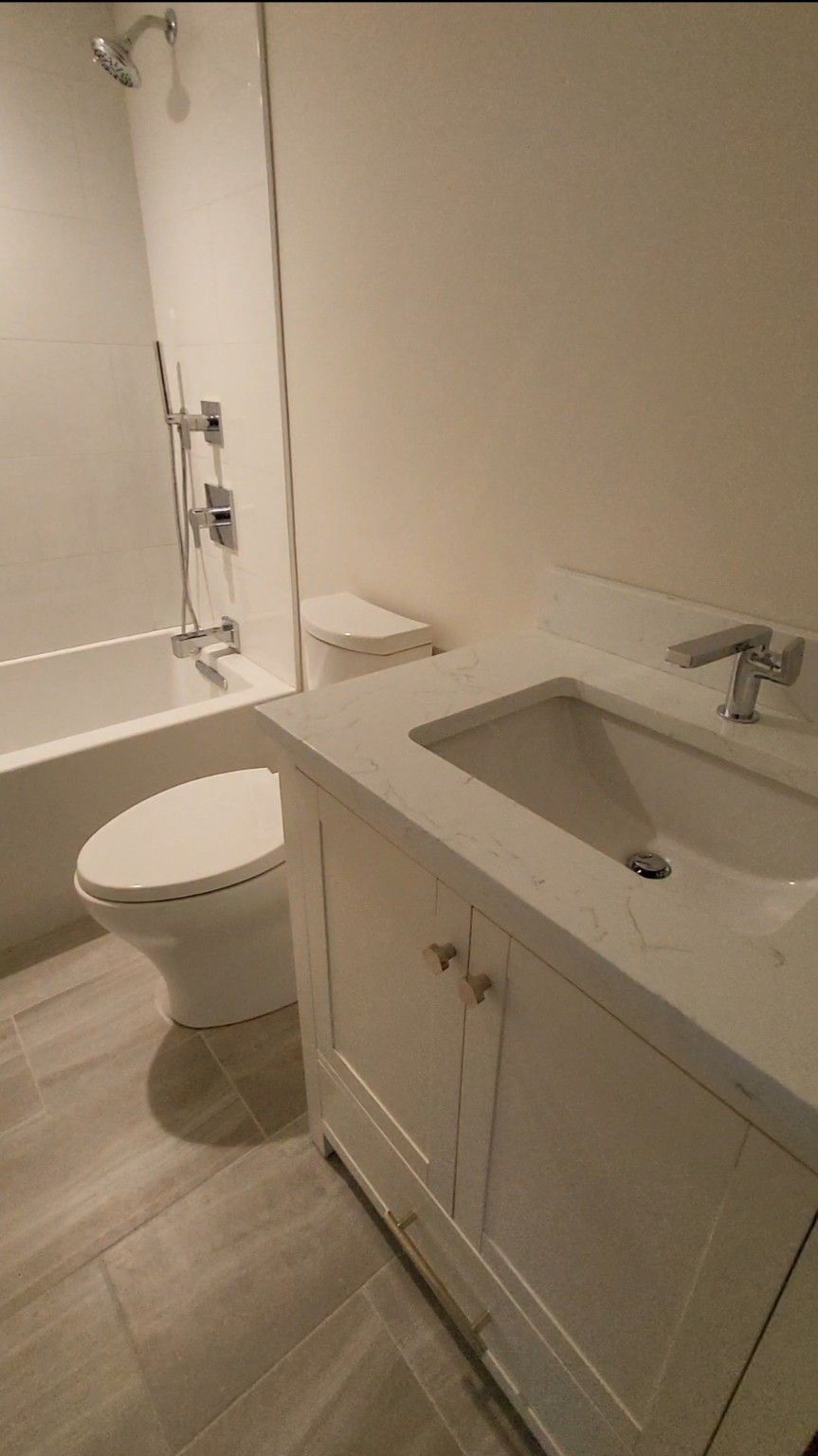 Before-and-after bathroom view: old shower area beside a newly tiled toilet and shower stall.
