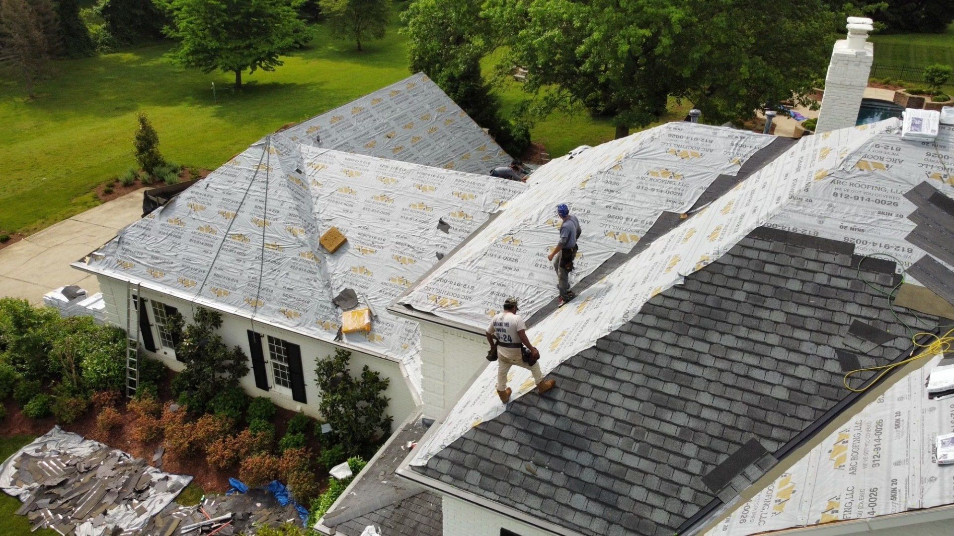 Two workers standing on gray roof with multiple layers covering roof — Georgetown, IN — ARC Roofing LLC