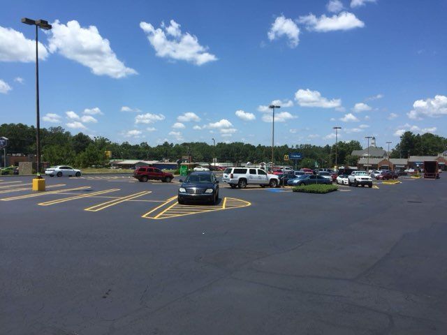 Wide parking lot with several cars under a blue sky with clouds, yellow-striped lanes in foreground