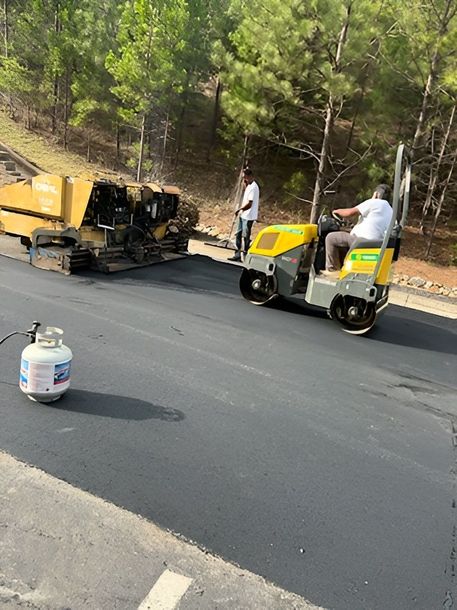 Road paving crew with yellow equipment spreading fresh asphalt on a rural road