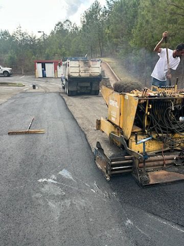 Road paving machine working on a fresh asphalt road with a worker standing nearby.