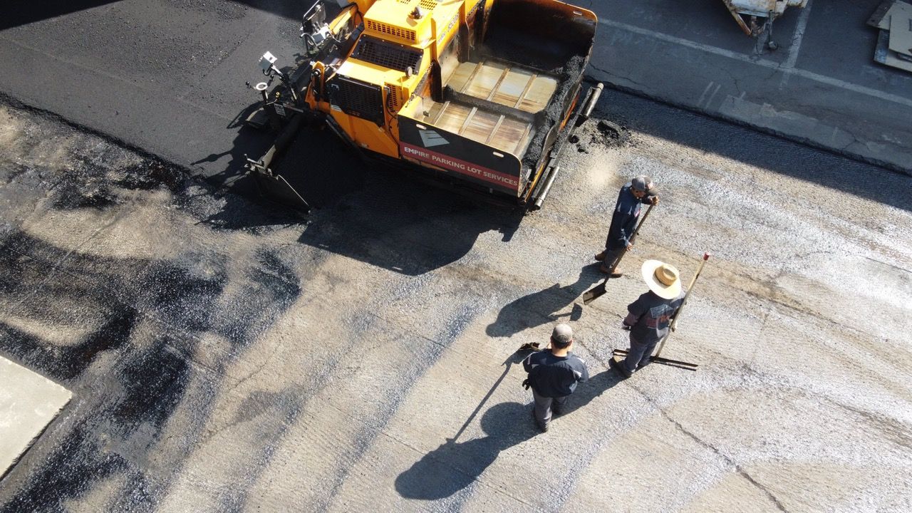 Road workers paving asphalt beside an orange paving machine on a sunlit street